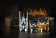 Drei Kristallgläser in verschiedenen Größen, elegant vor einem Kamin arrangiert, mit einem gemütlichen Sessel im Hintergrund.