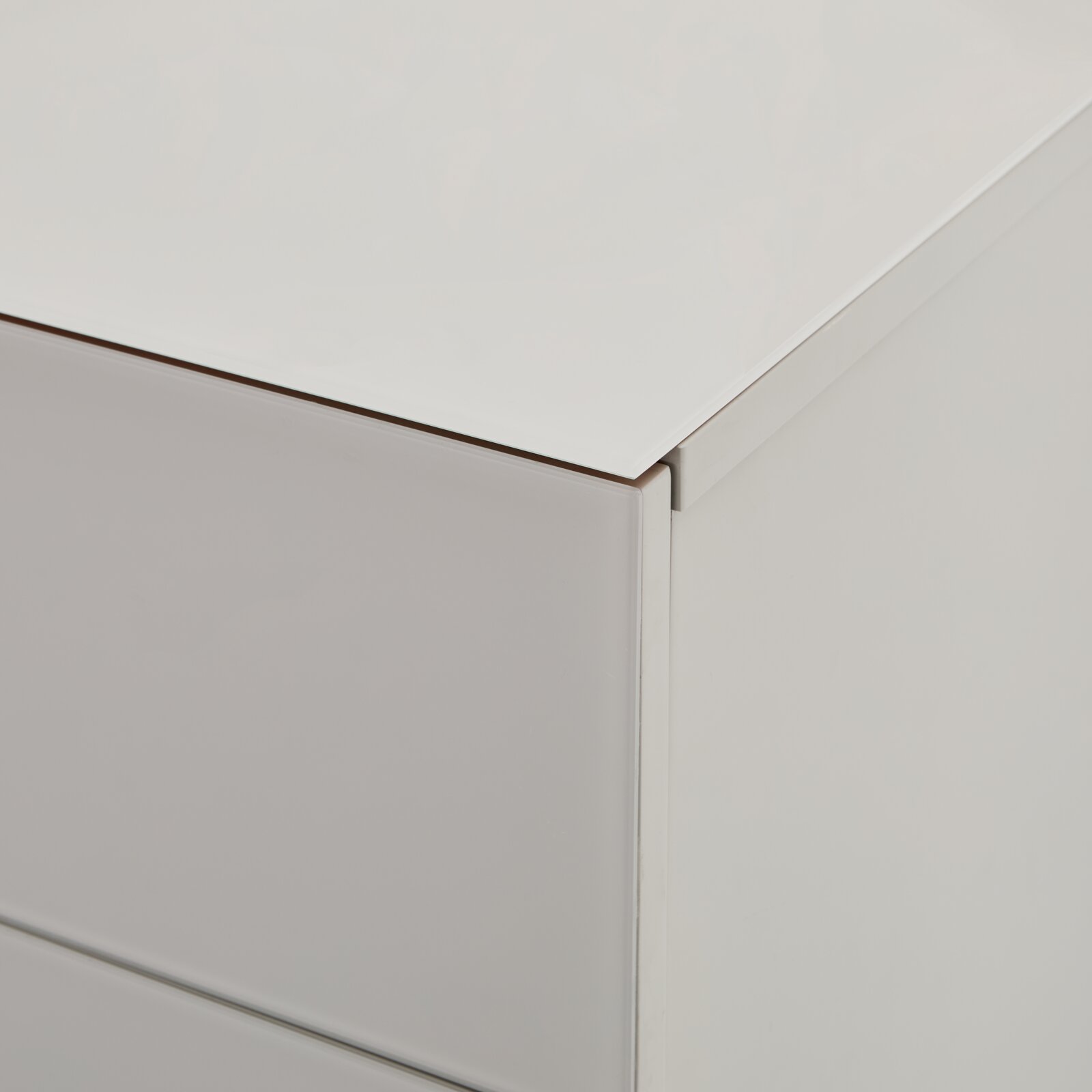Detailaufnahme einer weißen Kommode mit glatter Oberfläche und Schubladenfront, gezeigt aus schräger Seitenansicht von oben