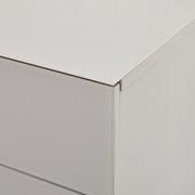 Detailaufnahme einer weißen Kommode mit glatter Oberfläche und Schubladenfront, gezeigt aus schräger Seitenansicht von oben