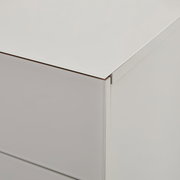 Detailaufnahme einer weißen Kommode mit glatter Oberfläche und Schubladenfront, gezeigt aus schräger Seitenansicht von oben