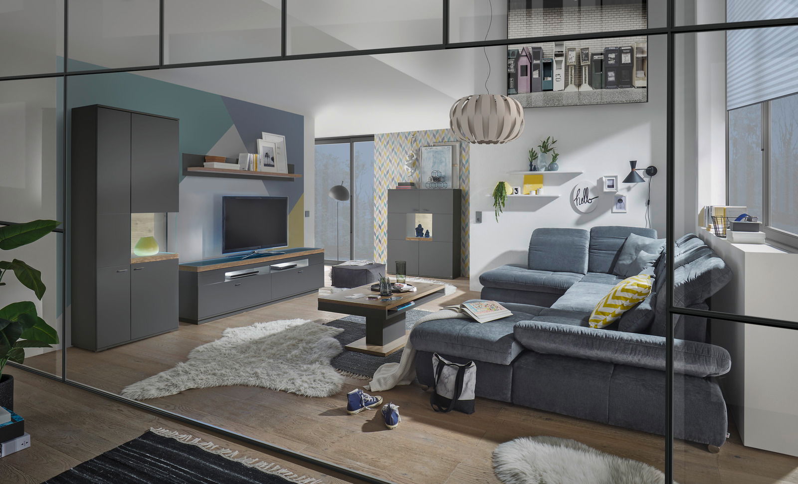 Moderne Wohnzimmeransicht mit grauem Sofa, Couchtisch, TV-Lowboard und Vitrine, aus der Perspektive durch eine Glastür betrachtet.