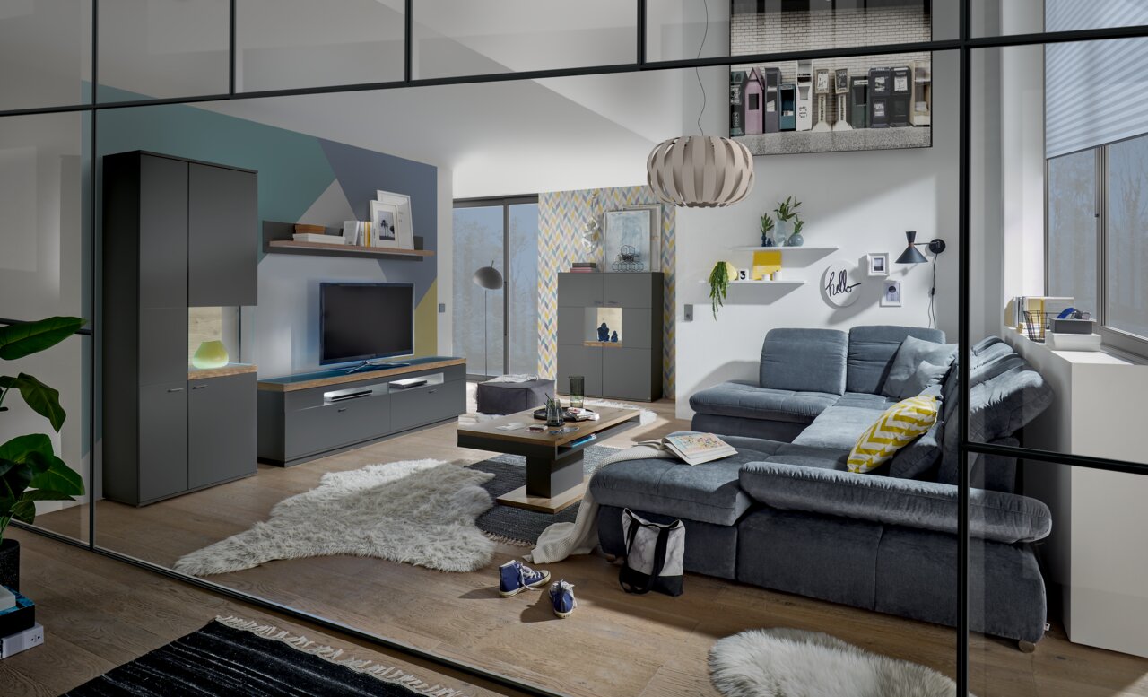 Moderne Wohnzimmeransicht mit grauem Sofa, Couchtisch, TV-Lowboard und Vitrine, aus der Perspektive durch eine Glastür betrachtet.