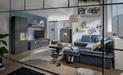 Moderne Wohnzimmeransicht mit grauem Sofa, Couchtisch, TV-Lowboard und Vitrine, aus der Perspektive durch eine Glastür betrachtet.