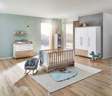 Modernes Babyzimmer mit Wickelkommode, Babybett, Wandregal und dreitürigem Kleiderschrank in Holz- und Weißtönen, seitliche Perspektive