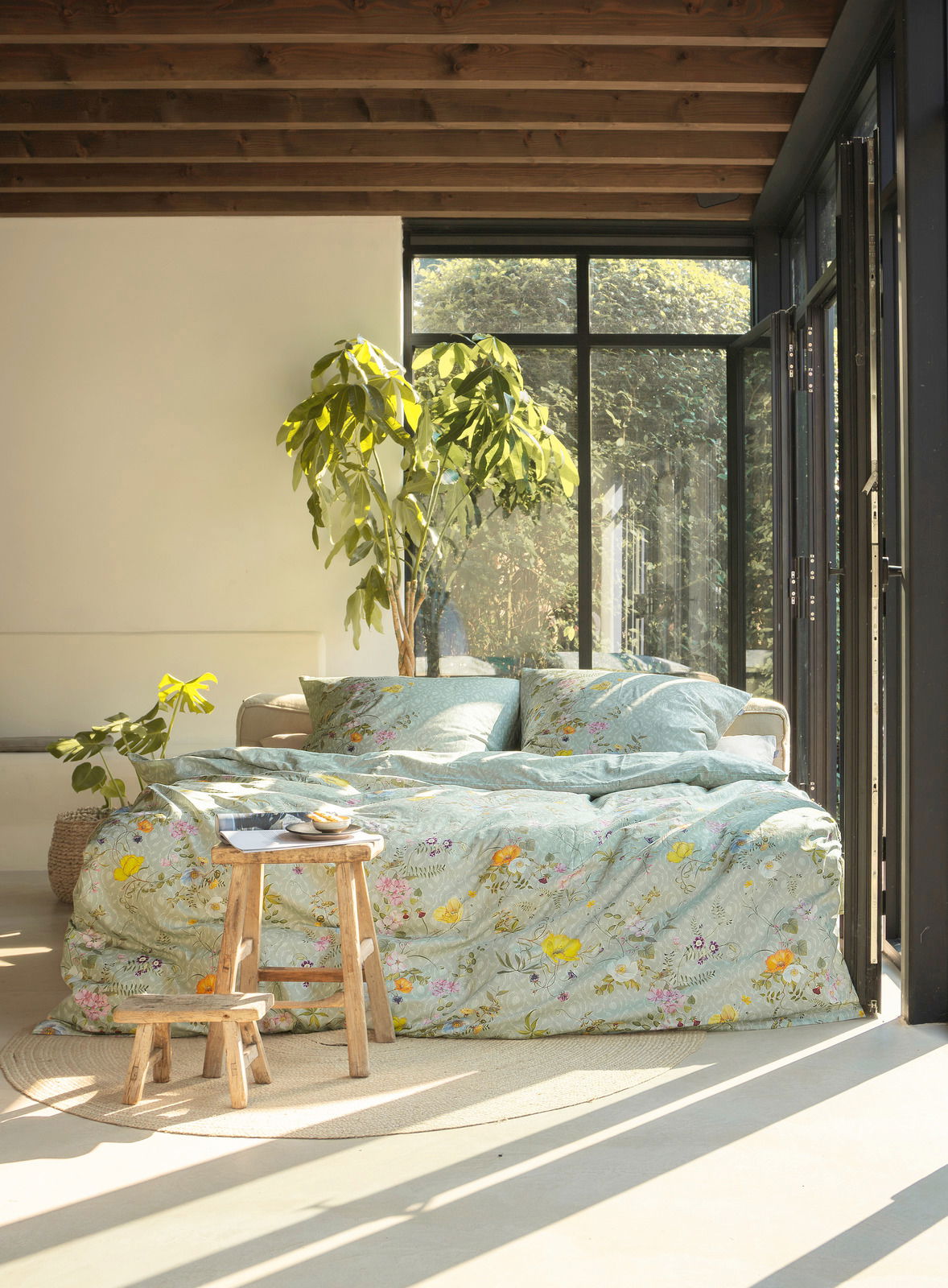 irisette Bettwäsche TOKIO Gemütliches Schlafzimmer mit Bettwäsche in floralen Mustern, Tageslicht durch große Fenster, Pflanzen im Hintergrund, seitliche Perspektive.