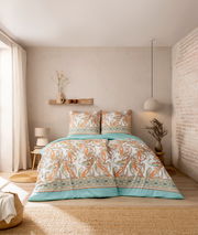 Bettwäsche-Set in einem gemütlichen Schlafzimmer, mit Paisley-Muster in Orange und Grün auf weißem Hintergrund, aus der Perspektive von vorne aufgenommen.