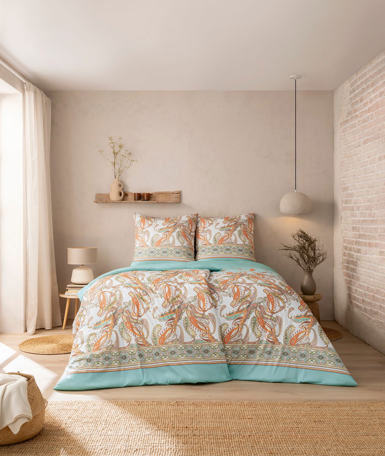 Estella Bettwäsche SIENA Bettwäsche-Set in einem gemütlichen Schlafzimmer, mit Paisley-Muster in Orange und Grün auf weißem Hintergrund, aus der Perspektive von vorne aufgenommen.