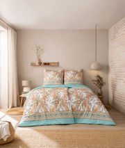 Bettwäsche-Set in einem gemütlichen Schlafzimmer, mit Paisley-Muster in Orange und Grün auf weißem Hintergrund, aus der Perspektive von vorne aufgenommen.