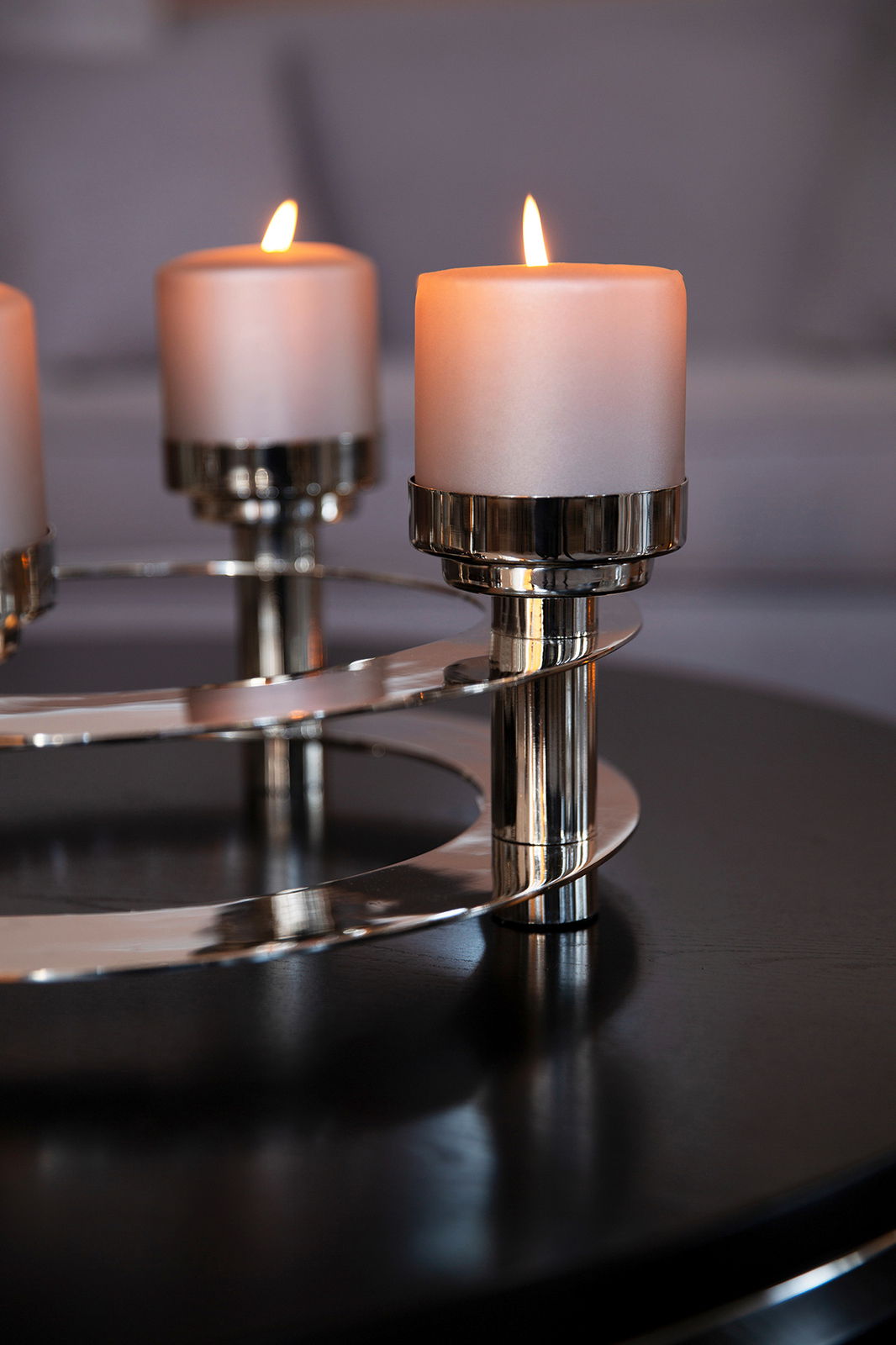 Nahaufnahme eines modernen, vierflammigen Kerzenleuchters aus Metall mit brennenden Kerzen auf einem Tisch.