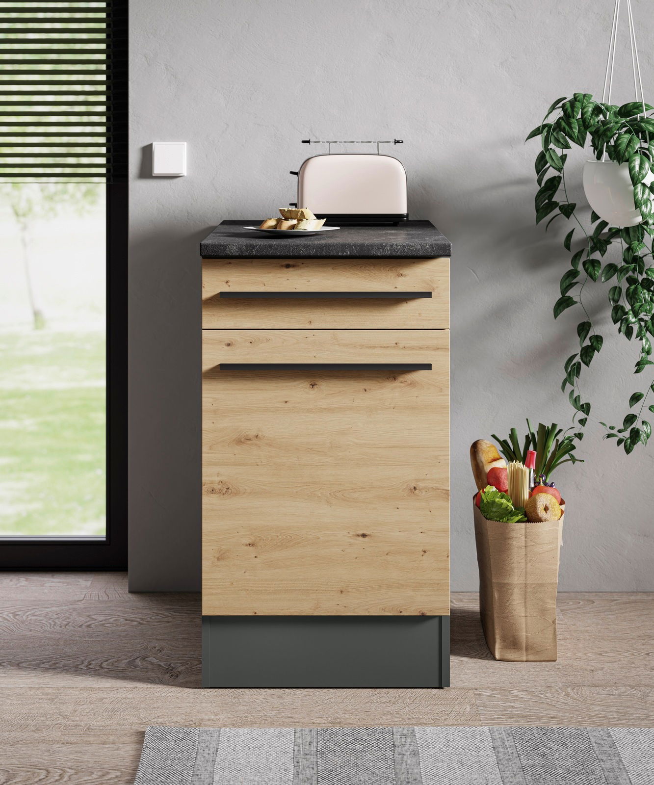 Moderner Unterschrank in Holzoptik mit schwarzer Arbeitsplatte, frontal fotografiert, mit Toaster und Obstkorb daneben.