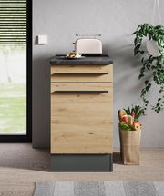 Moderner Unterschrank in Holzoptik mit schwarzer Arbeitsplatte, frontal fotografiert, mit Toaster und Obstkorb daneben.