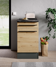 Moderner Unterschrank in Holzoptik mit schwarzer Arbeitsplatte, frontal fotografiert, mit Toaster und Obstkorb daneben.