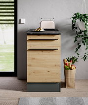 Moderner Unterschrank in Holzoptik mit schwarzer Arbeitsplatte, frontal fotografiert, mit Toaster und Obstkorb daneben.