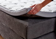 Nahaufnahme eines Boxspringbetts mit einer Hand, die die Matratze anhebt, um die Struktur und den Bezug zu zeigen.