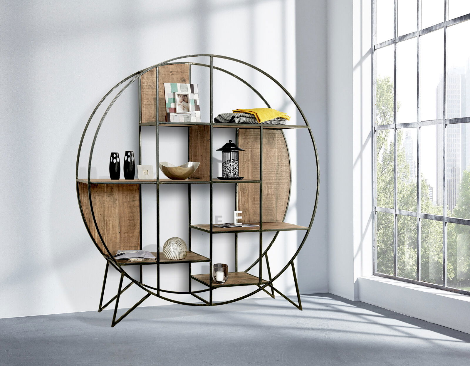Landscape Regal rund SPRING Rundes Regal aus Metall und Holz, seitliche Perspektive, mit dekorativen Gegenständen gefüllt, in einem hellen Raum mit großen Fenstern.