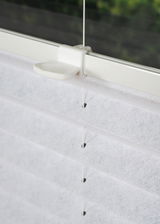 Nahaufnahme eines weißen, gefädelten Plissees an einem Fenster, seitliche Perspektive