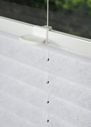 Nahaufnahme eines weißen, gefädelten Plissees an einem Fenster, seitliche Perspektive