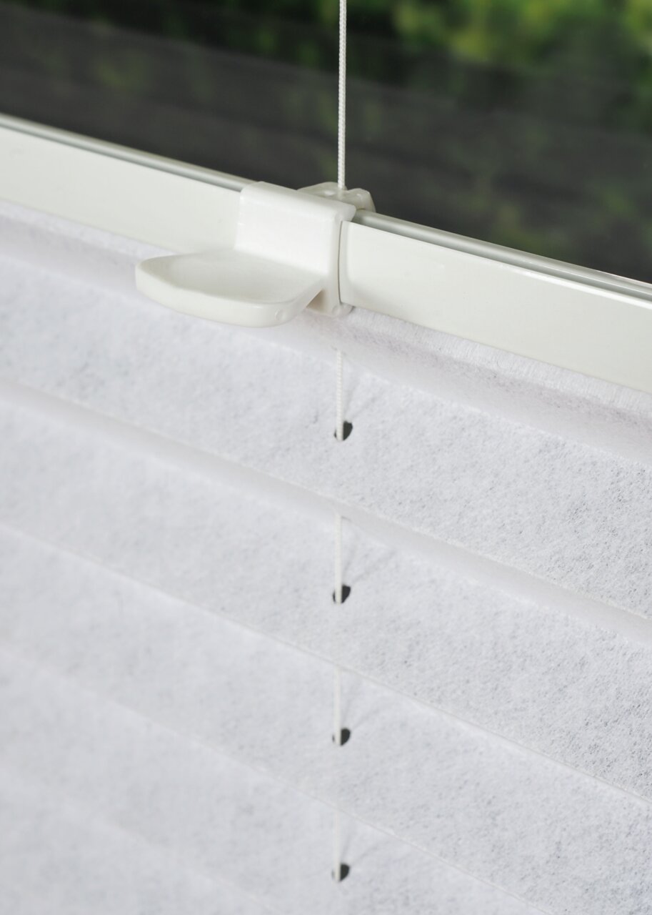 Nahaufnahme eines weißen, gefädelten Plissees an einem Fenster, seitliche Perspektive