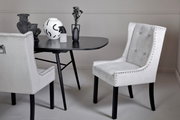 Eleganter weißer Stuhl mit Nietenverzierung, seitliche Perspektive, neben einem modernen schwarzen Tisch mit dekorativen Vasen.