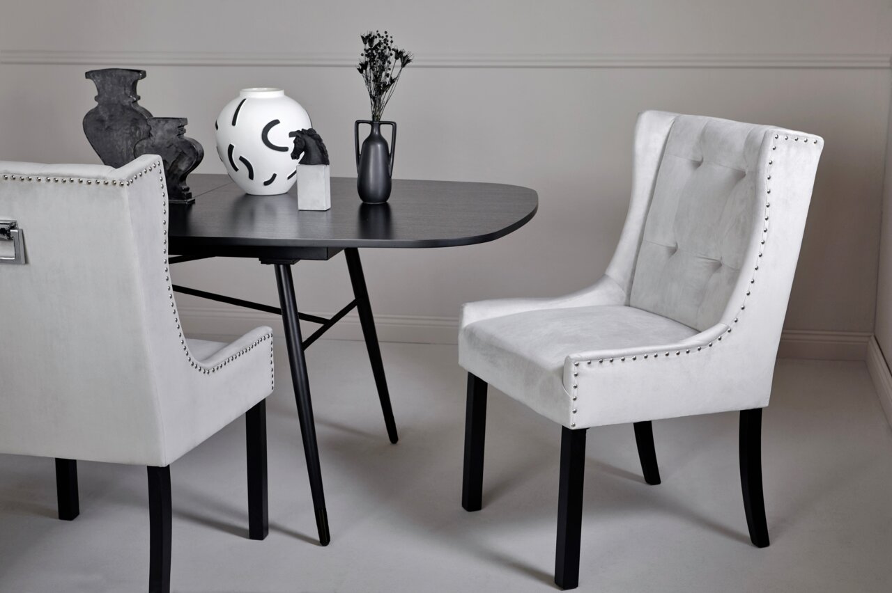 Jahnke Stuhl SAVIK Eleganter weißer Stuhl mit Nietenverzierung, seitliche Perspektive, neben einem modernen schwarzen Tisch mit dekorativen Vasen.
