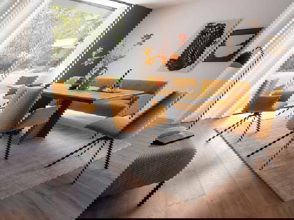 Ein modernes Esszimmer mit Holztisch, senfgelben Stühlen, Bank und großer Fensterfront mit Gartenblick.