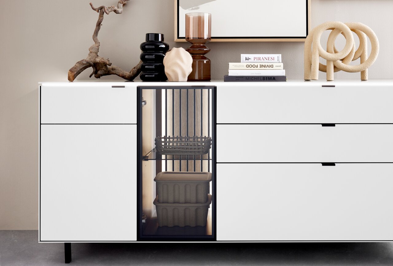 Modernes weißes Sideboard mit dekorativen Objekten und Büchern auf der Oberseite, frontal betrachtet.