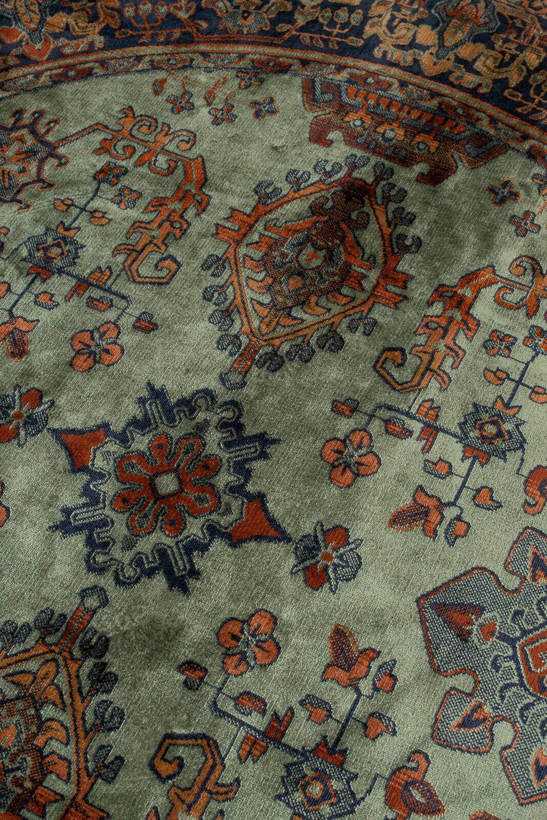 Nahaufnahme eines Teppichs mit traditionellem Muster in Rot- und Blautönen auf grünem Hintergrund, aus schräger Perspektive fotografiert.