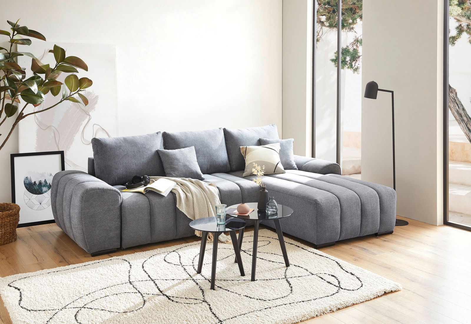 Graue Rundecke in modernem Wohnzimmer, seitliche Perspektive, mit Kissen und Couchtisch auf hellem Teppich.