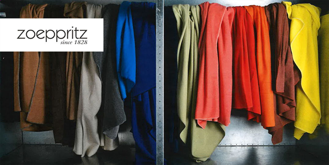 Bunte Decken oder Stoffe hängen ordentlich sortiert in einem offenen Metallschrank.