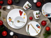 Draufsicht auf ein festlich dekoriertes Porzellan-Geschirrset in Weiß mit weihnachtlichen Motiven (Herzen, Sterne, Engel und Strümpfe), bestehend aus Teller, Schalen und Tassen, arrangiert auf Jute mit goldfarbenem Besteck, roten Äpfeln, Tannenzapfen und 