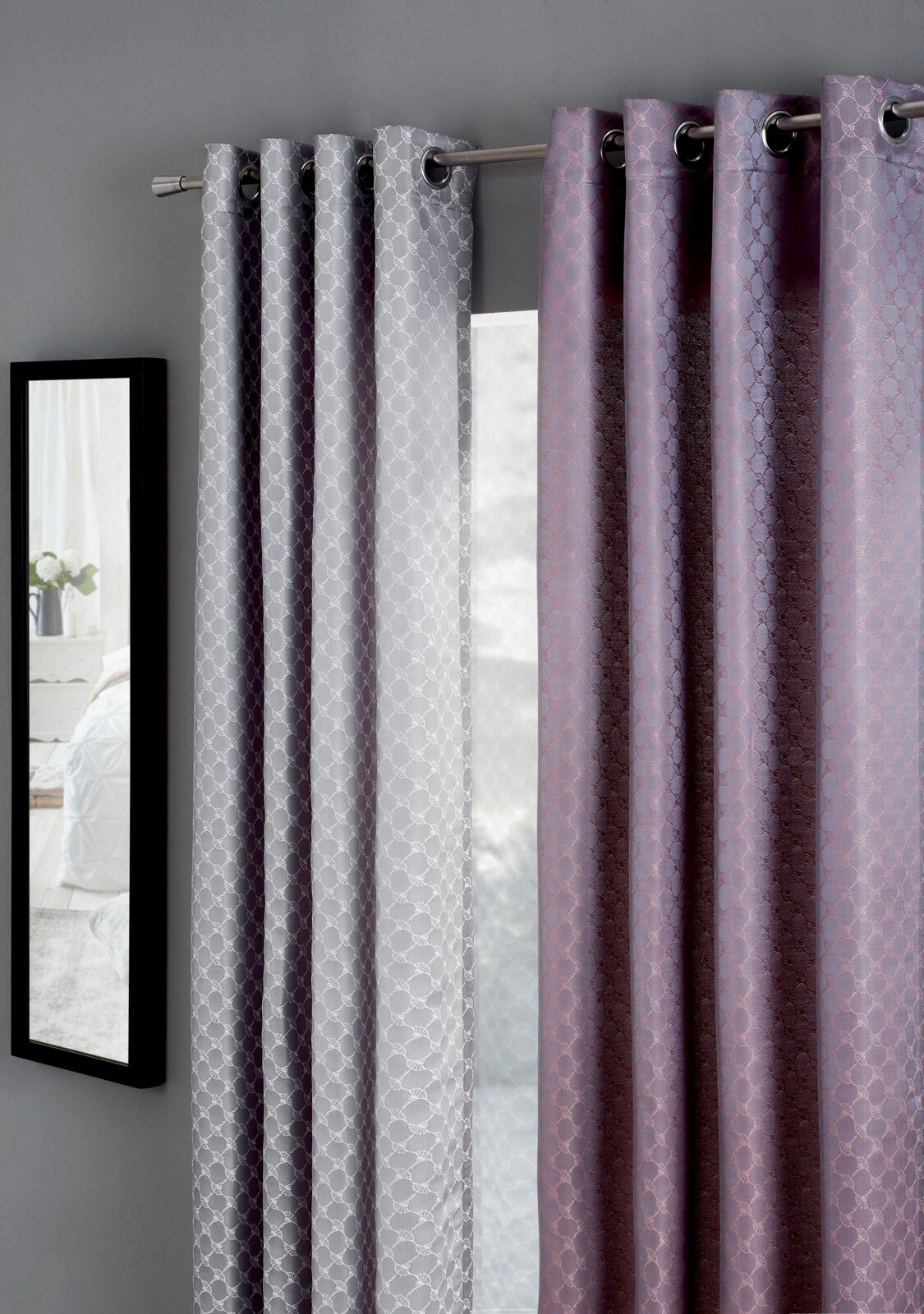 JOOP! Ösenschal J!Allover Zwei Vorhänge in Grau und Lila mit geometrischem Muster, aufgehängt an einer Gardinenstange, seitliche Perspektive.