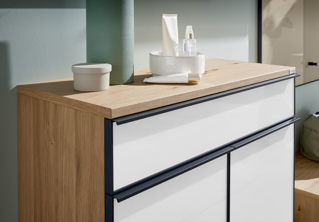 Nahaufnahme eines modernen Schuhschranks mit Holzoberfläche und weißen Fronten, dekoriert mit kleinen Behältern und Pflegeprodukten.