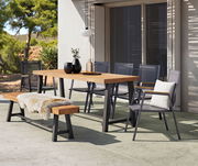Moderner Gartentisch mit Holzplatte und Metallgestell, umgeben von stilvollen Stühlen und einer Bank mit Fellauflage, in einer sonnigen Terrassenumgebung.