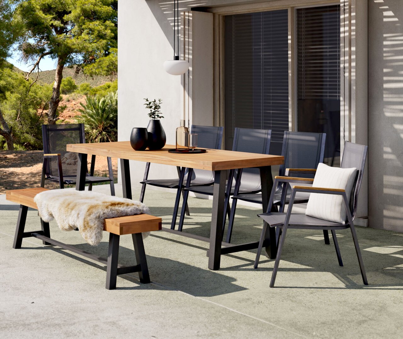 Ambia Garden Gartenbank SPLITWORK Moderner Gartentisch mit Holzplatte und Metallgestell, umgeben von stilvollen Stühlen und einer Bank mit Fellauflage, in einer sonnigen Terrassenumgebung.