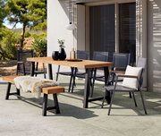 Moderner Gartentisch mit Holzplatte und Metallgestell, umgeben von stilvollen Stühlen und einer Bank mit Fellauflage, in einer sonnigen Terrassenumgebung.