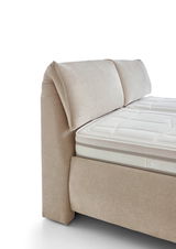 Seitliche Ansicht eines beigen Polsterbetts mit gepolstertem Kopfteil und Matratze.