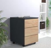 Moderner Rollcontainer mit drei Schubladen, schwarzem Korpus und Holzfronten, in schräger Vorderansicht von links in einem hellen Wohn-/Büroambiente.