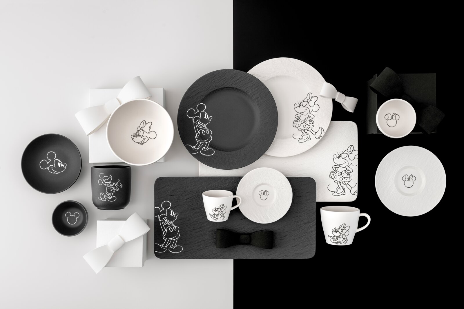 Schwarz-weißes Disney-Micky-und-Minnie-Mouse-Geschirrset mit Tellern, Schalen, Tassen und Servierbrett, flach von oben (Top-Down) fotografiert auf zweigeteiltem hell/dunklem Hintergrund.