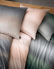 Bettwäsche-Set mit Farbverlauf in Grau, Rosa und Grün, mit 'bugatti' Schriftzug, aus der Vogelperspektive fotografiert.