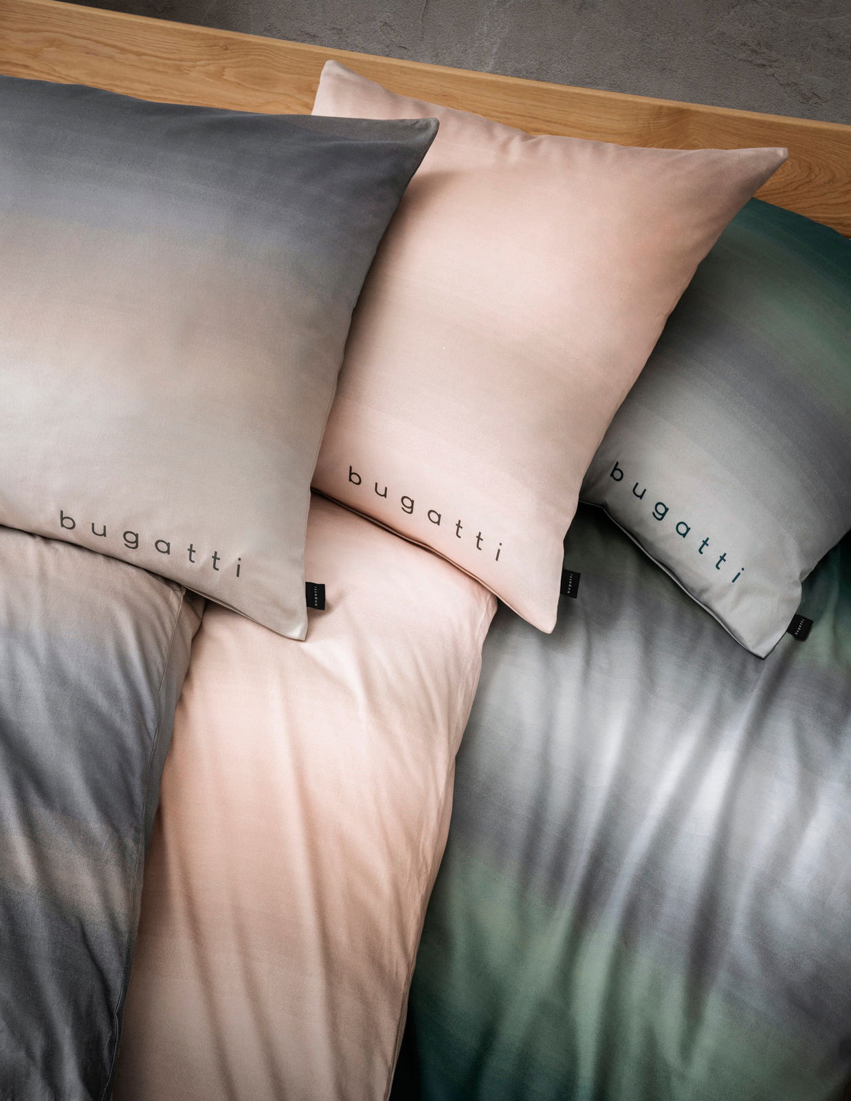 Bettwäsche-Set mit Farbverlauf in Grau, Rosa und Grün, mit 'bugatti' Schriftzug, aus der Vogelperspektive fotografiert.