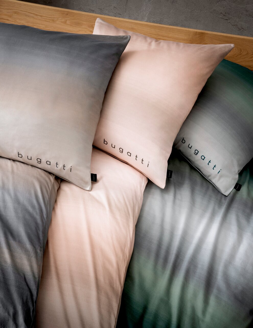 Bettwäsche-Set mit Farbverlauf in Grau, Rosa und Grün, mit 'bugatti' Schriftzug, aus der Vogelperspektive fotografiert.