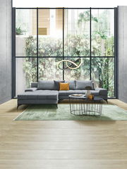 Graue Rundecke OttliZ2 FIGARO in modernem Wohnzimmer mit großem Fenster im Hintergrund, seitliche Perspektive.
