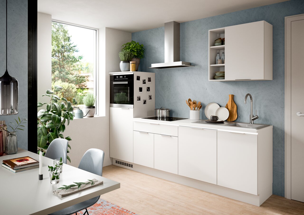 Moderne weiße Küchenzeile mit Herd, Spüle und Hängeschränken, seitliche Perspektive mit Blick auf ein großes Fenster und Pflanzen.