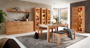 Wohnzimmer mit modernen Holzmöbeln, darunter ein Sideboard, Vitrinen und ein Esstisch mit Bänken, aus einer frontalen Perspektive fotografiert.