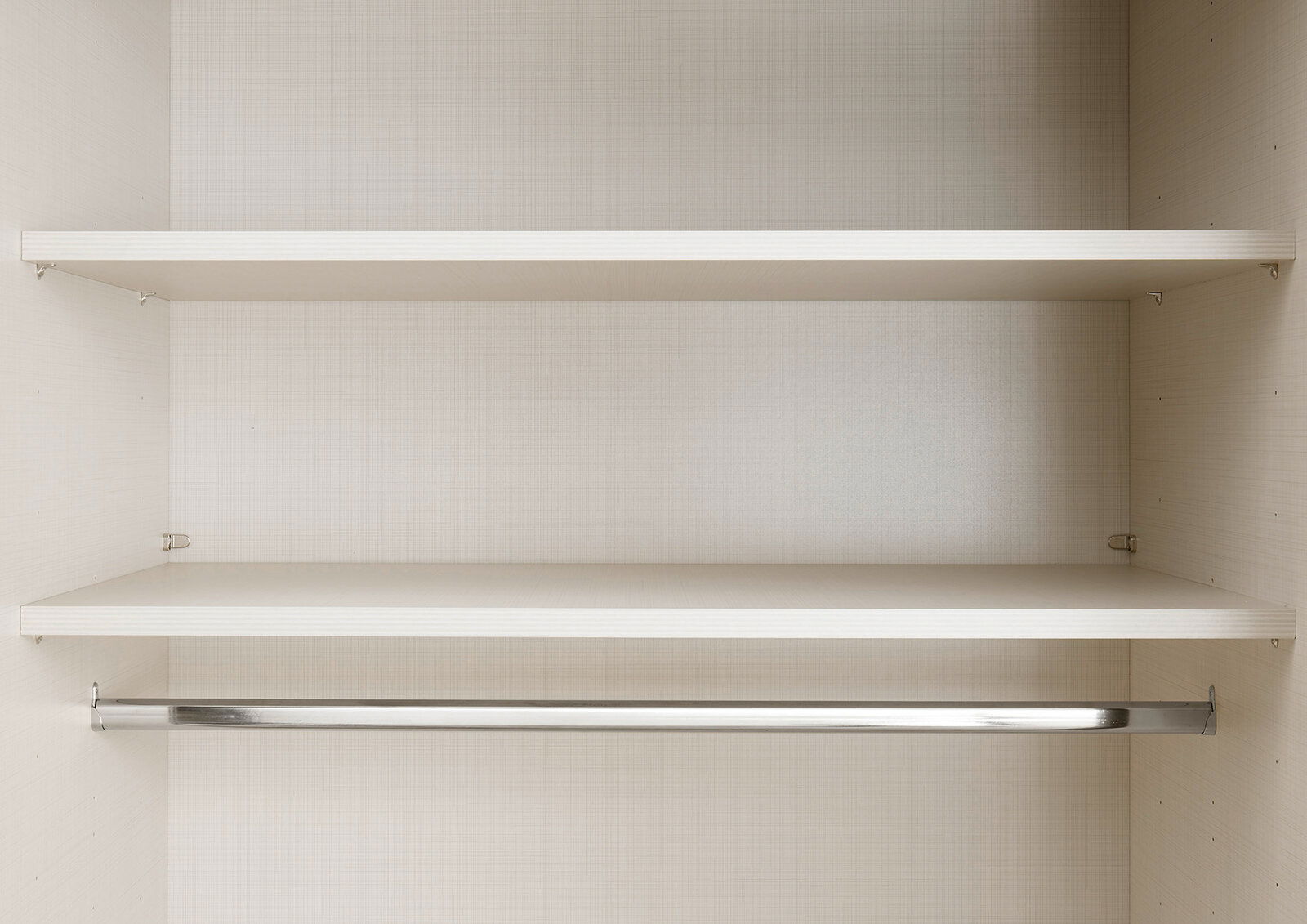 Innenansicht eines Schwebetürenschranks mit zwei Regalböden und einer Kleiderstange, frontal betrachtet.