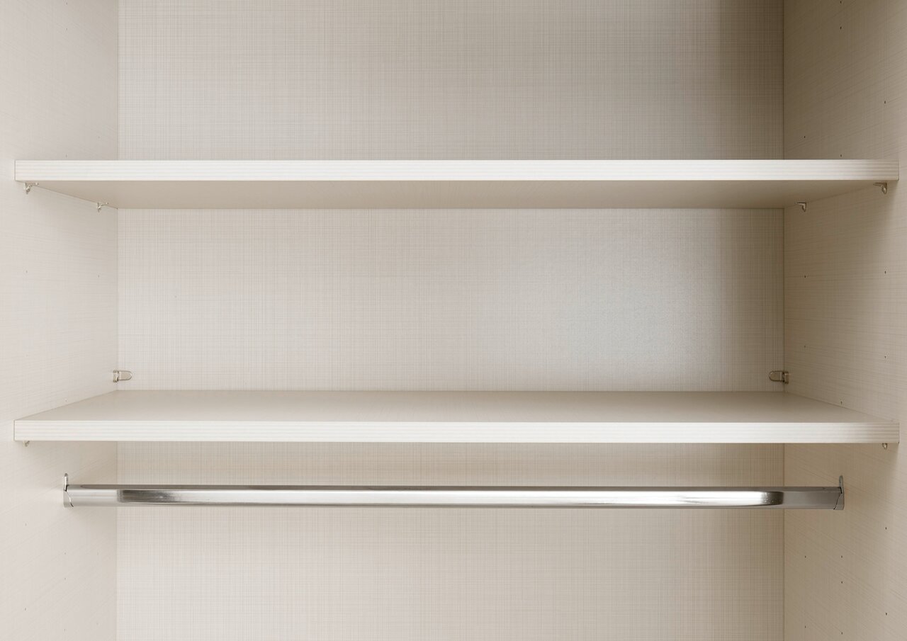 Innenansicht eines Schwebetürenschranks mit zwei Regalböden und einer Kleiderstange, frontal betrachtet.