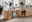 Moderner Schreibtisch aus Holz mit schwarzem Metallrahmen, ausgestattet mit Schubladen und Regalfächern, in einem hellen Büro mit Pflanzen und Dekorationen. Perspektive von vorne links.