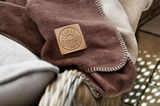 Nahaufnahme einer braunen Wohndecke mit einem Söller Home Logo, drapiert über einem Korbstuhl.