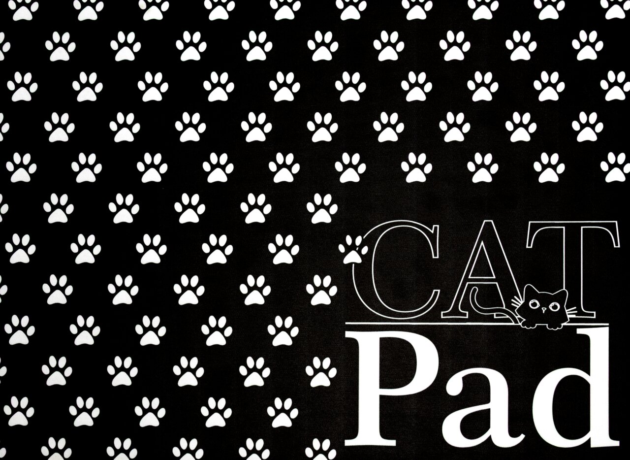 Stuco Fressnapfunterlage CAT PAD Schwarze Fressnapfunterlage mit weißen Pfotenabdrücken und der Aufschrift 'CAT Pad', von oben betrachtet.
