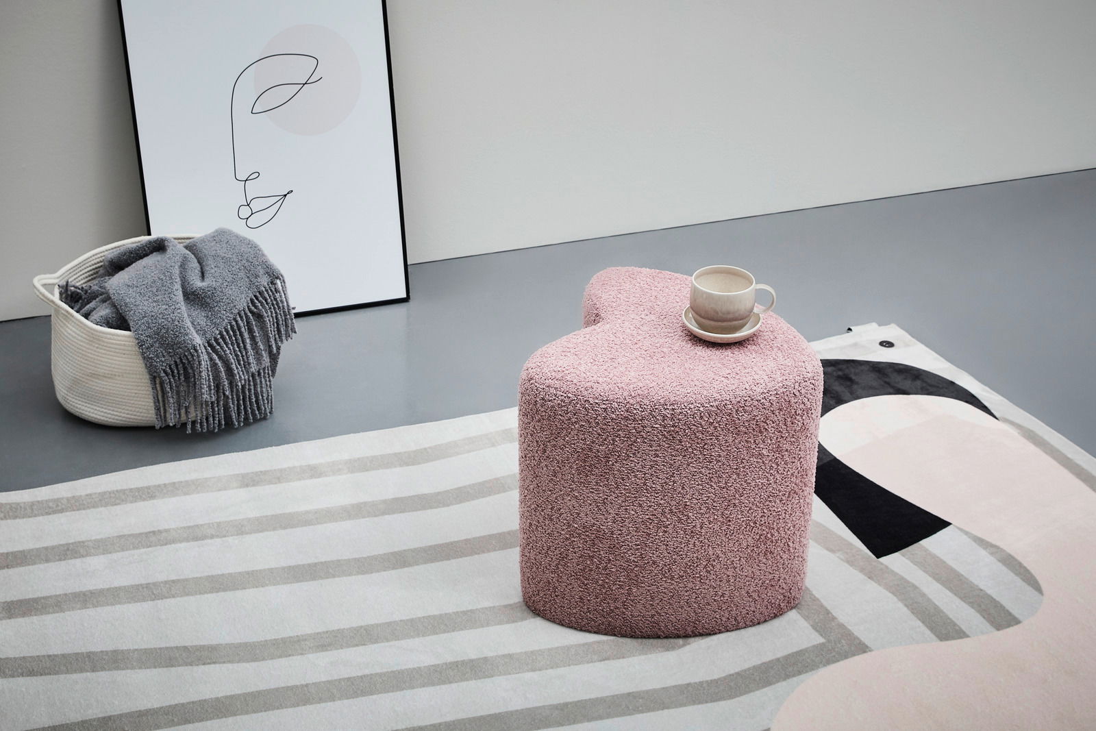 Rosa Hocker in Herzform, von schräg oben fotografiert, mit einer Tasse darauf, auf einem gemusterten Teppich.